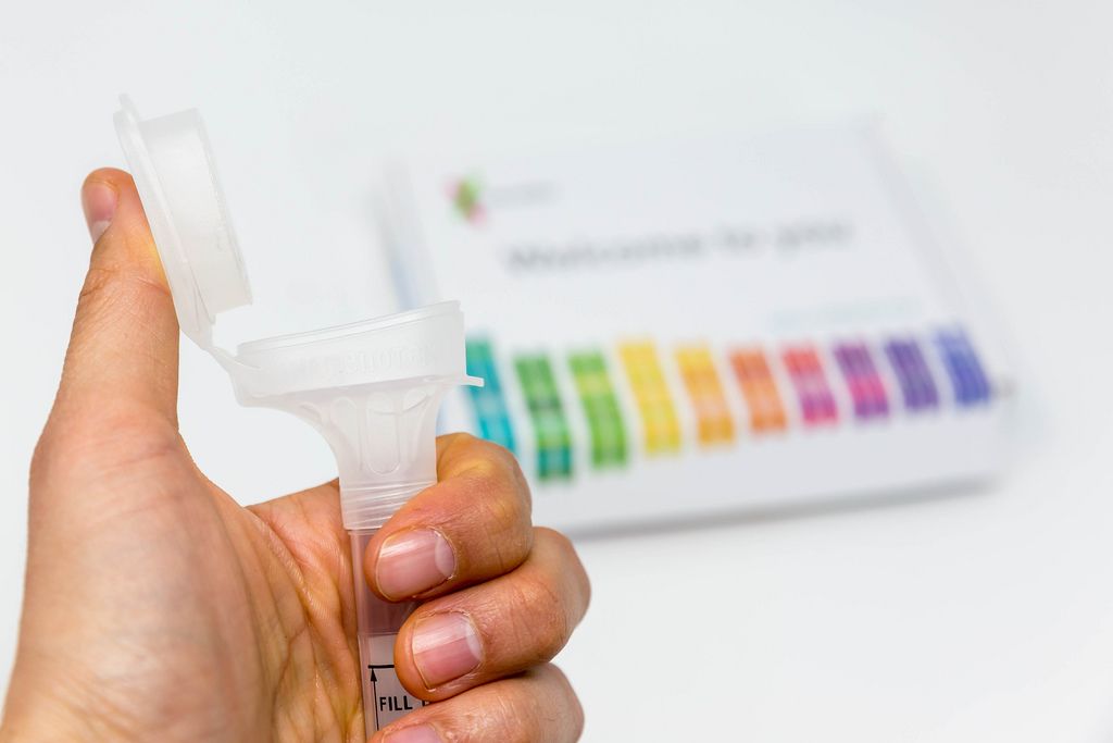 hand-holds-saliva-collection-kit-tube-from-23andme-with-open-funnel-lid-to-test-health-and-ancestry-with-personal-genetic-in-front-of-blurry-background